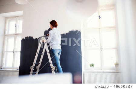 A young woman painting wall black. A startup of small business. A young woman painting wall black. A startup of small business. 49650237