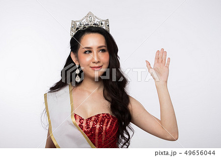 Portrait of Miss Asian Pageant Beauty Contest in Red sequin Evening Ball Gown long dress with sparkle light Diamond Crown, Most Beautiful Woman wave hand to camera, studio lighting white background 49656044