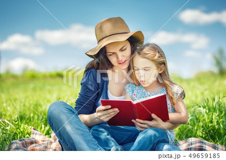 Mother and daughter reading book on green summer meadow 49659185