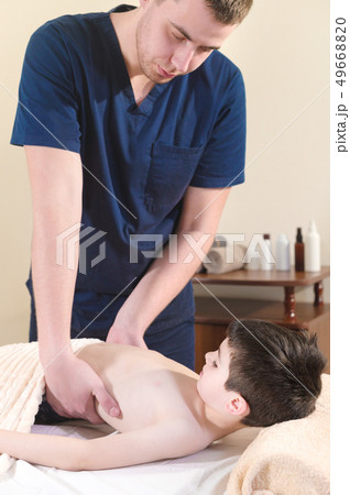 A male physiotherapist masseur makes a healing relaxing massage to a little smiling boy lying on a 49668820