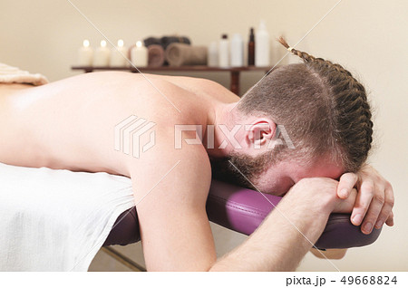 Male hipster with braided trendy hair and shaved temples lying on a massage bunk down face resting Male hipster with braided trendy hair and shaved temples lying on a massage bunk down face resting 49668824