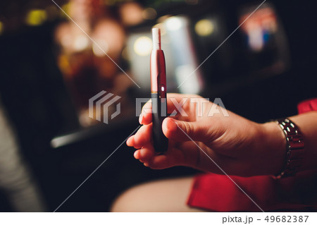 Electronic cigarettes, technology cigarette. Tobacco system IQOS. Female hand on blurred background Electronic cigarettes, technology cigarette. Tobacco system IQOS. Female hand on blurred background 49682387
