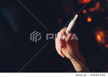 Electronic cigarettes, technology cigarette. Tobacco system IQOS. Female hand on blurred background Electronic cigarettes, technology cigarette. Tobacco system IQOS. Female hand on blurred background 49683490