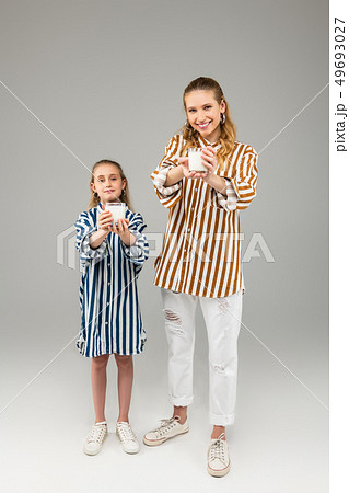 Pleasant smiling ladies in bright striped shirts showing glasses in their hands Pleasant smiling ladies in bright striped shirts showing glasses in their hands 49693027