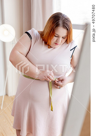 Unhappy plump woman looking at the centimeter tape 49707480