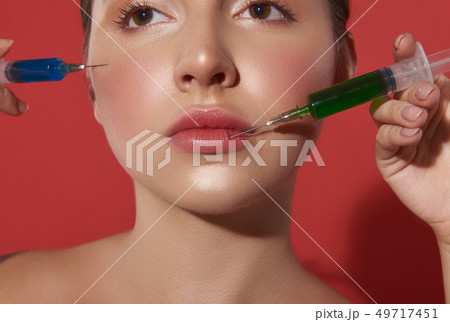 Face of young woman with two syringes near it Face of young woman with two syringes near it 49717451