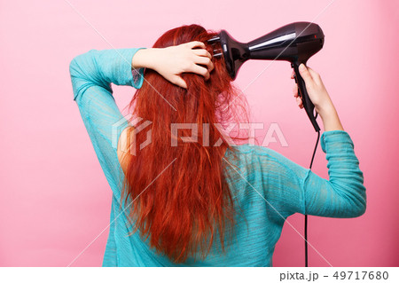 Woman holding a hairdryer on a pink background 49717680