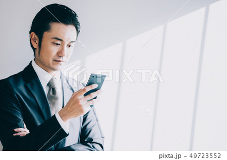 携帯電話を見ながら白壁を背景に立つ上司の男性 携帯電話を見ながら白壁を背景に立つ上司の男性 49723552