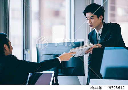 デスク越しに資料を手渡す上司と部下の男性 デスク越しに資料を手渡す上司と部下の男性 49723612