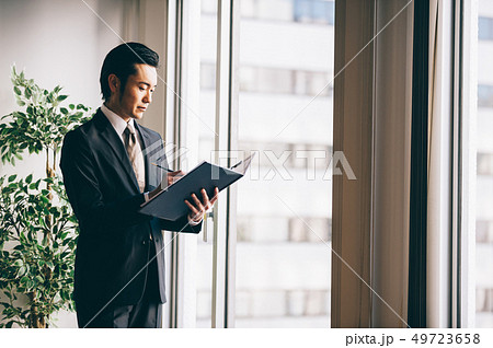 窓際でファイルを手にメモを取る上司の男性 窓際でファイルを手にメモを取る上司の男性 49723658