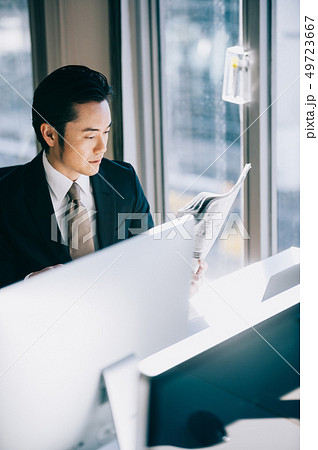 窓際の席でパソコンに向かい新聞を読む上司の男性 窓際の席でパソコンに向かい新聞を読む上司の男性 49723667