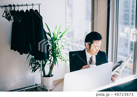 窓際の席でパソコンに向かい新聞を読む上司の男性 窓際の席でパソコンに向かい新聞を読む上司の男性 49723673