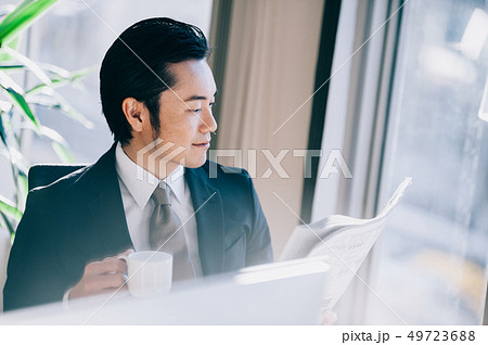 窓際の席でパソコンに向かい新聞を読む上司の男性 窓際の席でパソコンに向かい新聞を読む上司の男性 49723688