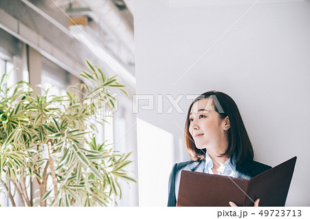 オフィスで柱にもたれファイルを確認する女性 49723713