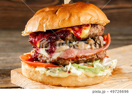 A big burger with two beef cutlets, cooked on charcoal. Lunch on a wooden background. The concept of A big burger with two beef cutlets, cooked on charcoal. Lunch on a wooden background. The concept of 49726696
