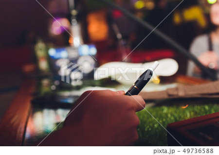 IQOS heat-not-burn tobacco product technology. Woman holding e-cigarette in his hand before smoking. IQOS heat-not-burn tobacco product technology. Woman holding e-cigarette in his hand before smoking. 49736588