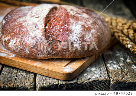 Round bread and wheat ears on the old wooden table Round bread and wheat ears on the old wooden table 49747025