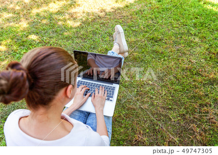 Young woman sitting on green grass lawn in city Young woman sitting on green grass lawn in city 49747305
