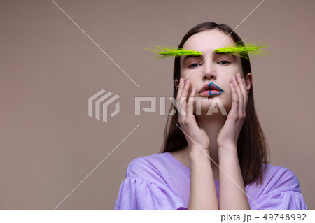 Woman having green spikelet on eyebrows touching her face Woman having green spikelet on eyebrows touching her face 49748992