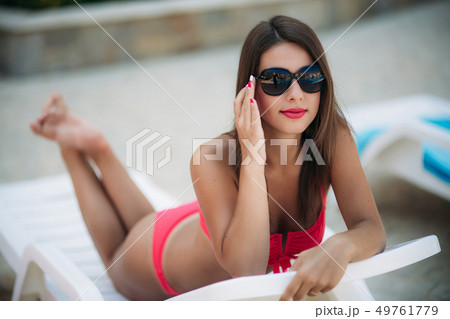 Beautiful lady in sunglasses lies on a sunbed in front of the pool 49761779
