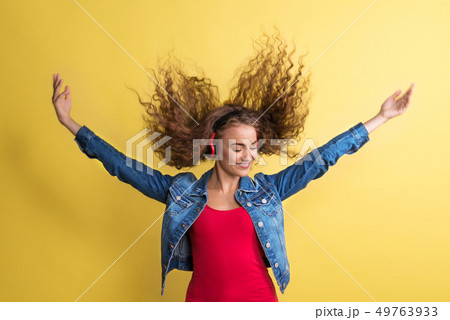 Portrait of a young woman with headphones in a studio on a yellow background. 49763933