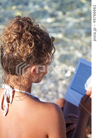 Woman with an e-reader on vacation at the beach Woman with an e-reader on vacation at the beach 49766662