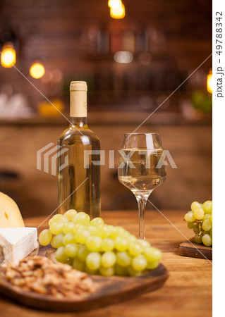 Bottle of white wine a glass full of it next to different cheeses 49788342