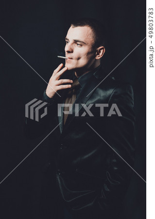 a young man smokes a cigarette, a black background, a classic black suit a young man smokes a cigarette, a black background, a classic black suit 49803783