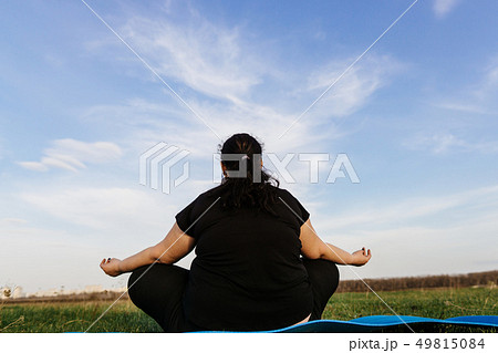 Overweight woman meditating at yoga mat outdoors 49815084