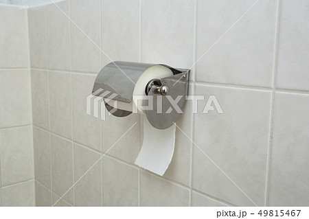 A white roll of soft toilet paper neatly hanging on a modern chrome holder on a light bathroom wall. 49815467