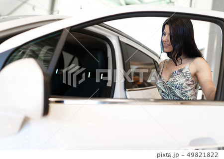 Beautiful fashionable brunet look at her new car in dealership showroom Beautiful fashionable brunet look at her new car in dealership showroom 49821822