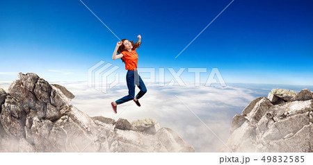 Redhead woman jumps over cliff on blue sky background. 49832585
