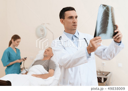 man lies on a cot. Doctor and a nurse help him. 49838009