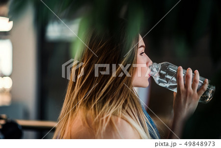 A side view of young girl or woman standing in a gym, drinking water. A side view of young girl or woman standing in a gym, drinking water. 49848973