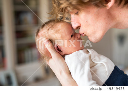 A young father holding a newborn baby at home, kissing him. A young father holding a newborn baby at home, kissing him. 49849423