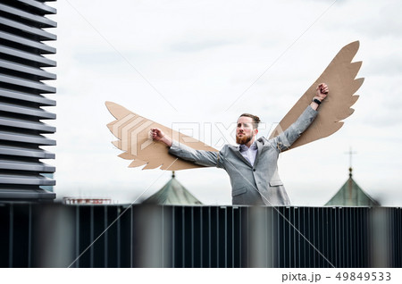 A young businessman with wings standing on a terrace, flying metaphor concept. A young businessman with wings standing on a terrace, flying metaphor concept. 49849533