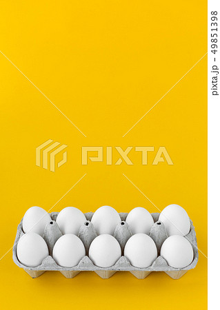 White hen eggs in open cardboard carton on yellow 49851398