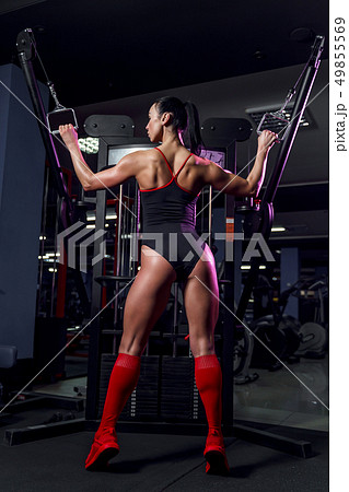 Athletic sexy woman doing exercise using machine in gym - back view 49855569