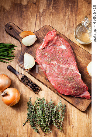 Raw beef steak on wooden cutting board next to onions and seasoned with rosemary 49866719