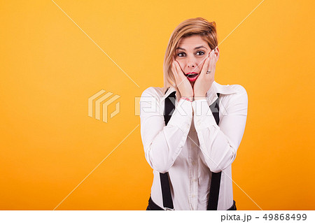 Attractive woman shocked and keeping hands on her cheeks over yellow background. Attractive woman shocked and keeping hands on her cheeks over yellow background. 49868499