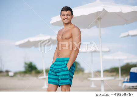 Man in shorts stand on the beach. Sun shines into his eyes and he squint 49869767