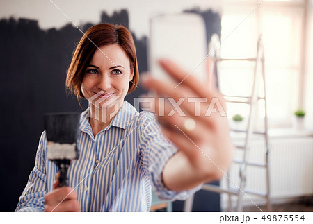 A portrait of young woman painting wall black, taking selfie. 49876554