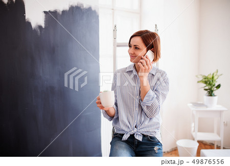 A portrait of young woman painting wall black. A startup of small business. 49876556