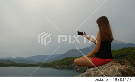 Female tourist sitting on a rock on clear sky and calm sea background Female tourist sitting on a rock on clear sky and calm sea background 49883477