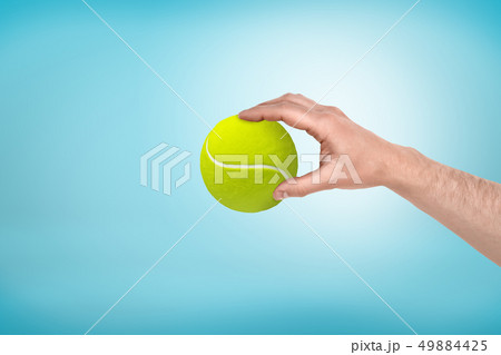 Male hand holding small tennis ball between fingers on blue background 49884425