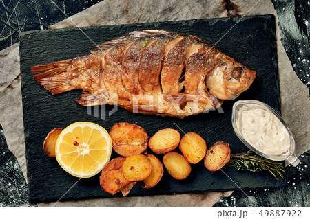 Grilled whole fish Served with baked potatoes, lemon and sauce. Top view. Grilled whole fish Served with baked potatoes, lemon and sauce. Top view. 49887922