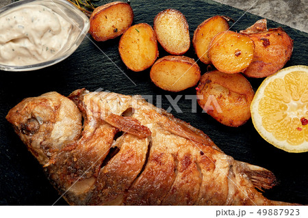 Grilled whole fish Served with baked potatoes, lemon and sauce. Top view. Grilled whole fish Served with baked potatoes, lemon and sauce. Top view. 49887923