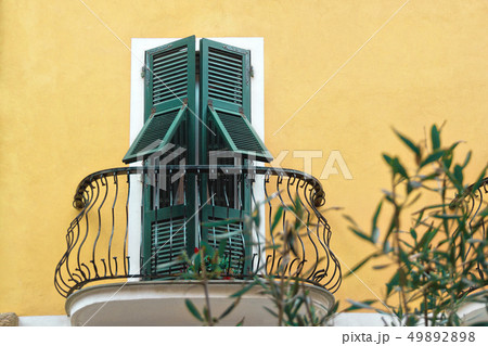 metallic black balcony with green wooden doors with shutters in white frame on yellow wall metallic black balcony with green wooden doors with shutters in white frame on yellow wall 49892898