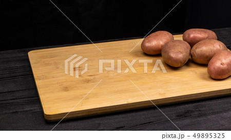 Potatoes on a cutting board prepared for cleaning and slicing. Ingredient for fried or boiled dishes Potatoes on a cutting board prepared for cleaning and slicing. Ingredient for fried or boiled dishes 49895325
