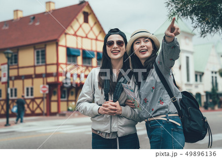 two happy friends holding map pointing outdoors 49896136
